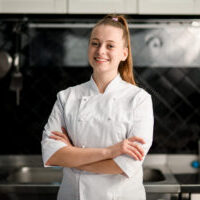 young beautiful smiling woman chef with arms crossed at kitchen